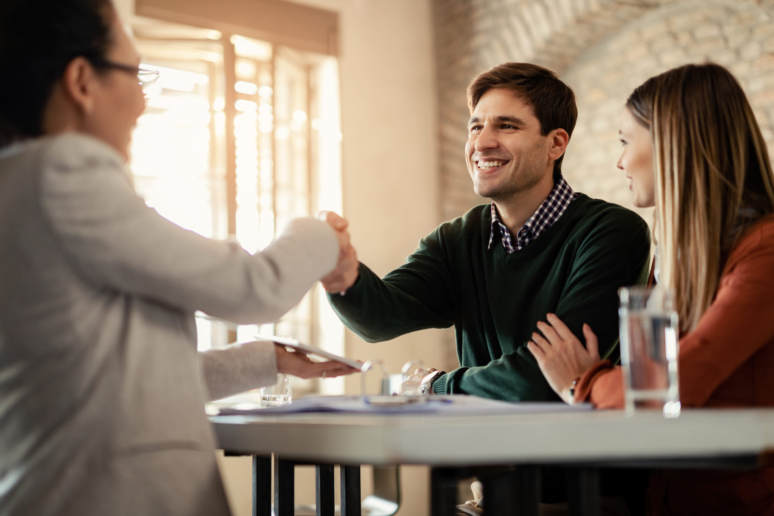 Happy couple shaking hands with financial advisor during a meeting in the office. Focus is on man.